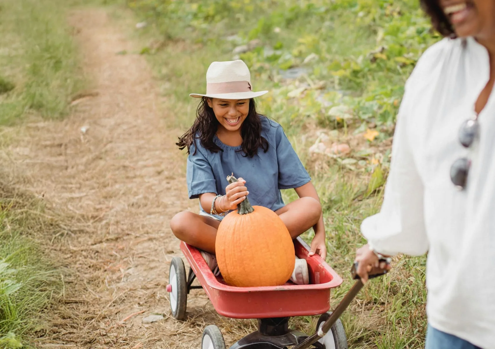 A child pulling a pumpkin in a red wagon.